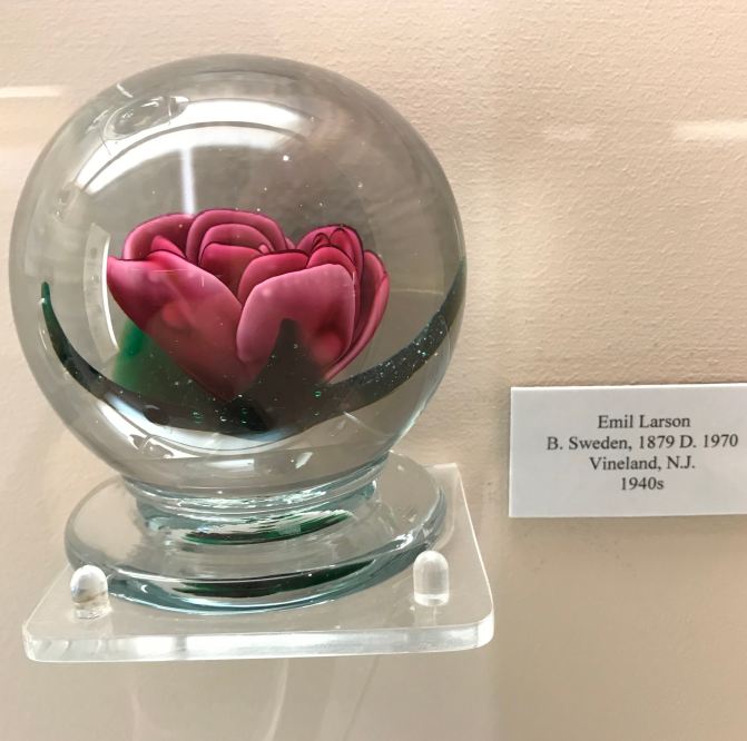 Round paperweight with rose glass decoration in middle. Sign on wall says EMIL LARSON b. SWEDEN 1879 D. 1970 VINELAND NJ 1940s