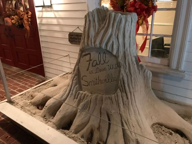 Sand sculpture of a tree trunk with the words FALL IN LOVE WITH SMITHVILLE carved on the trunk.