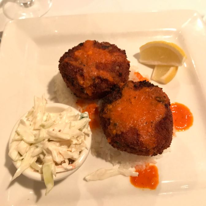 Crab cakes on plate with lemon slices and slaw.