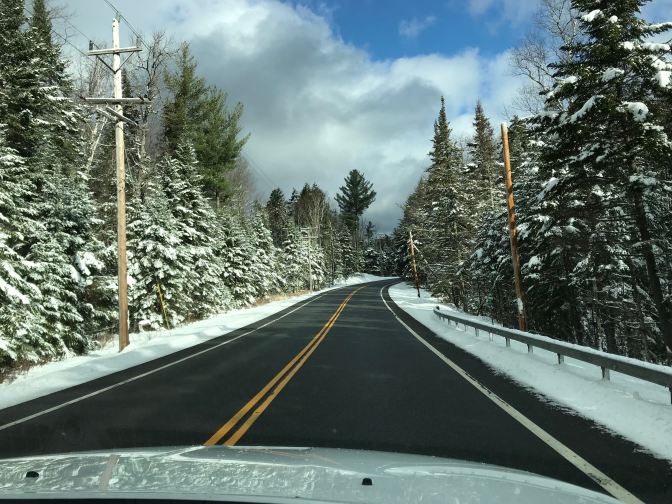 Sunny sky with clouds over snow-covered trees along a mountain road.