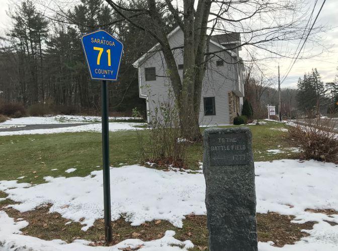 Stone marker along roadside that says TO THE BATTLEFIELD 1777. A road sign is beside it that says SARATOGA COUNTY 71.