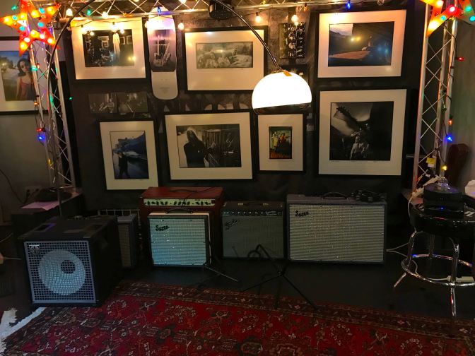 Stage with guitar amplifiers. Photographs hang from the wall behind the stage.