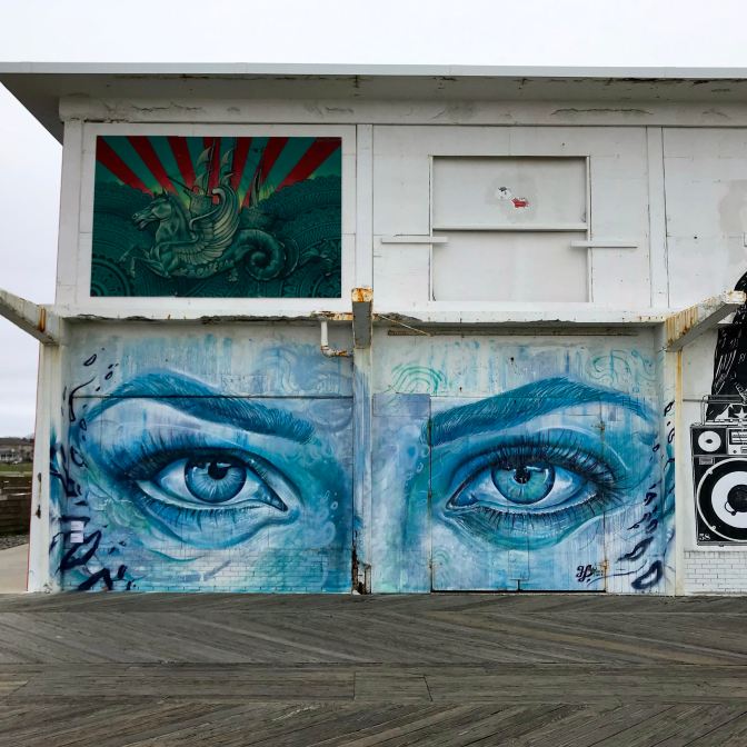 Mural of unicorn in front of sailing ship and another of face focused on two large eyes.