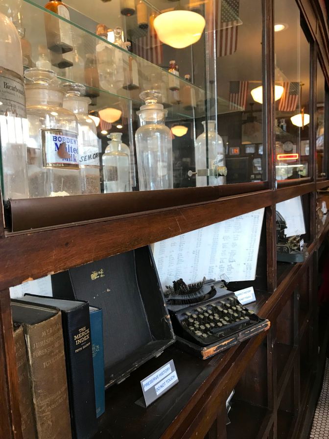 Wall lined with glass cases housing instruments and bottles of a historic pharmacy.