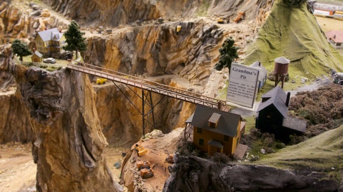 House on rocky pillar in a quarry pit, surrounded by mining operations on rim of crater.