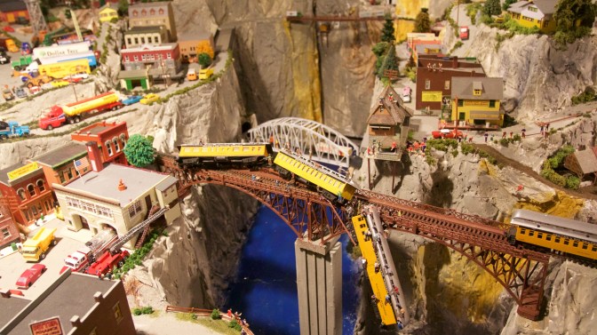 Diorama of town with railroad bridge across canyon, and a derailed train hanging off the bridge.