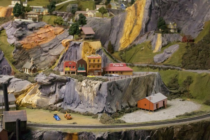 Mountain village scene, with a pizza hut model on the top of the hill, and several small cars around it.
