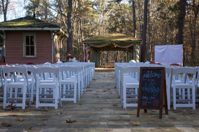 Outdoor wedding setup, with white chairs in rows before a small gazebo. A sign says WELCOME TO OUR WEDDING.