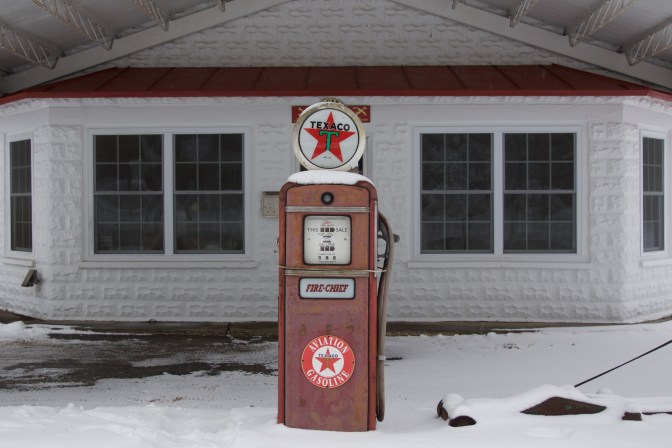 Old gas station, with a single red pump in the middle of the frame.