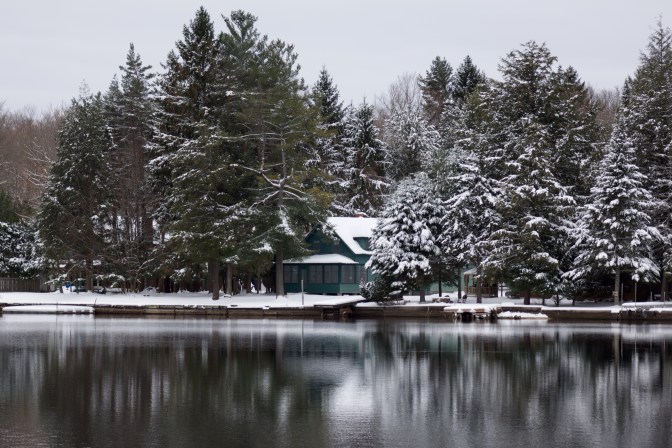 Cabin surrounded by snow-covered trees beside a lake.