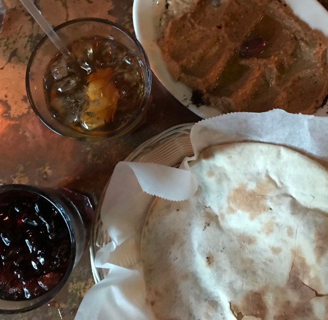Table with two drinks, pita, and baba ganoush.