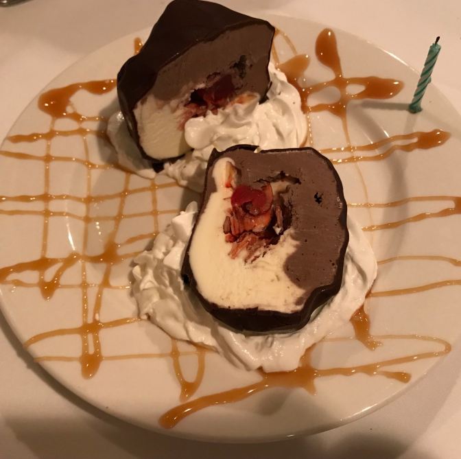 Chocolate and vanilla tartufo, with caramel drizzled across the plate. A candle is attached to the side of the plate.