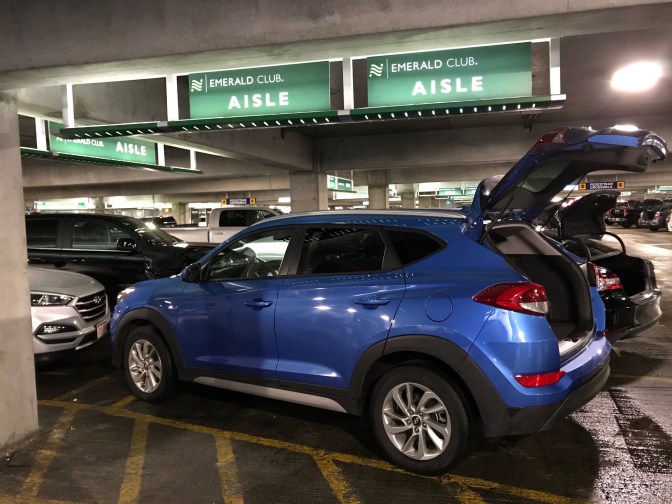 Blue Hyundai Tuscon in parking garage, signs above that says EMERALD CLUB AISLE.