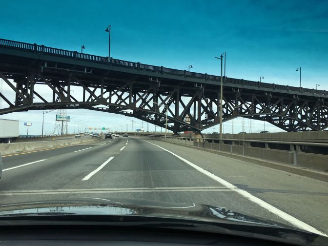 View of NJ Turnpike. A large metal bridge crosses the roadway.
