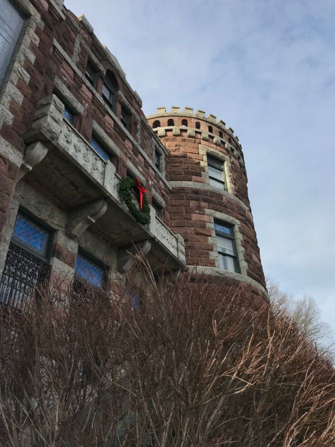 Exterior of castle, looking at three-story turret. Bare branches of a bush are in the foreground.