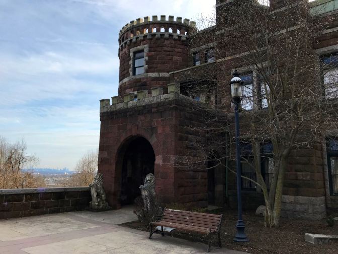 View of entrance to Lambert Castle, with skyline of New York in the distance.