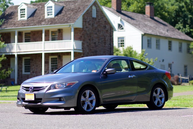 Side view of 2012 Honda Accord coupe, in gray ,with buildings in the background.