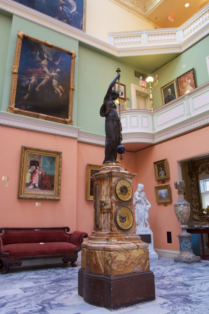 Grand Atrium, with a large clock statue in the middle of the floor, and paintings on the wall.