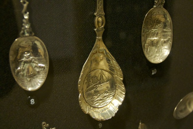 Close-up of pewter spoons with engravings. Center engraving has an ocean liner on the sea.