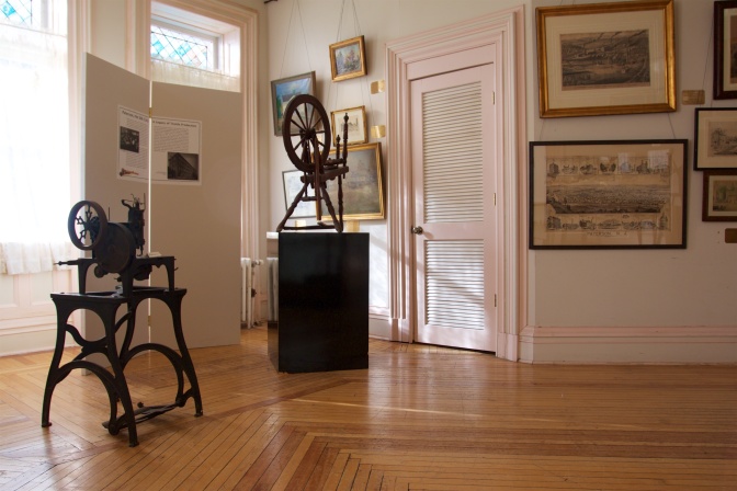 Spinning equipment on a wooden floor. Paintings hang along the walls.
