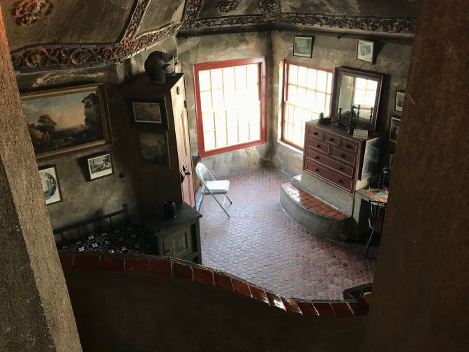 Guest room with windows in far corner, dressed, bed, and armoire. Paintings are hung on the walls.