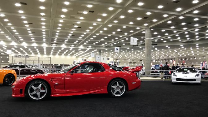 Red Mazda RX-7, with a white Corvette in the background on the right.