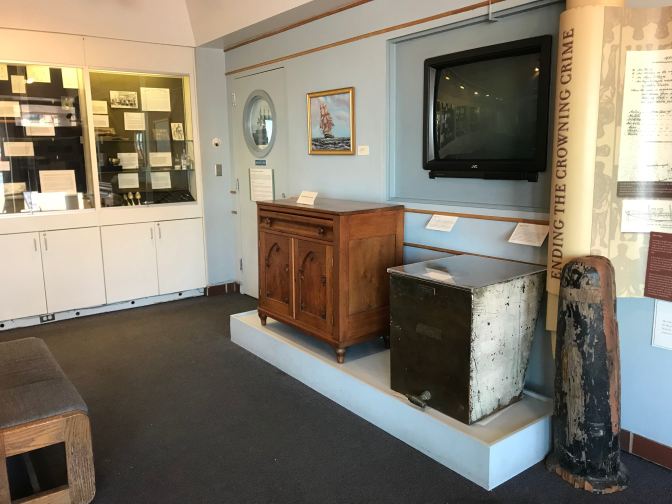 Museum at the USS Constellation featuring furniture from the ship, a TV, and display cases with items from the ship.