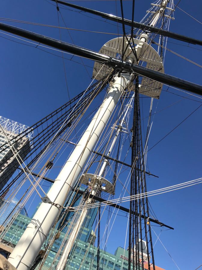 Looking upward at forward mast of ship, with rigging and ropes criss-crossing the image.