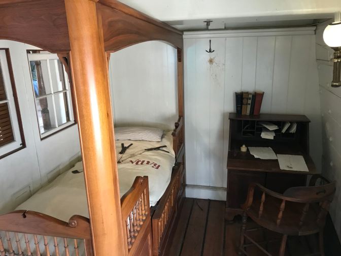 Captain's quarters, with a four-poster bed and a desk with a chair.