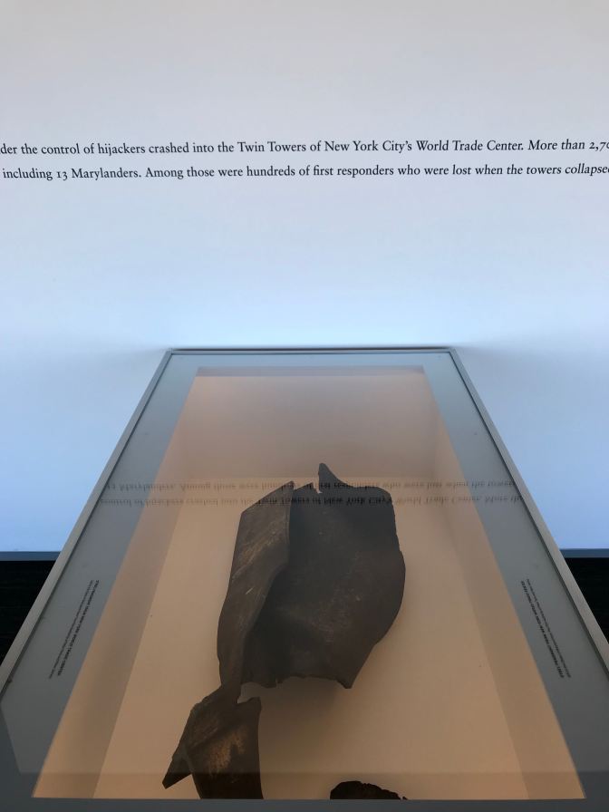 Display case with fragment of World Trade Center. Text on wall behind display tells story of 9/11.