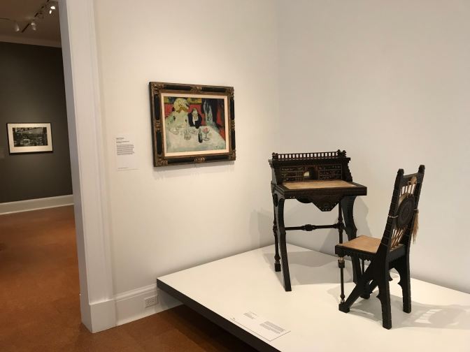 Desk and chair on a plinth in the museum, with a painting on the wall beside it.