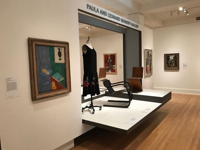 Dress on mannequin, two chairs, and four paintings, in a gallery.