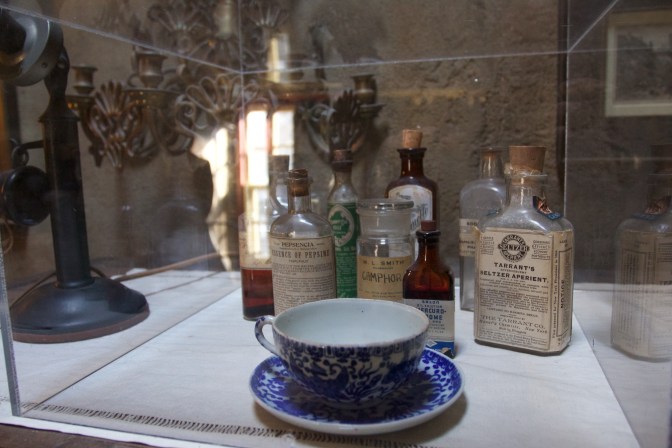 Medicines and a tea cup in a glass case.