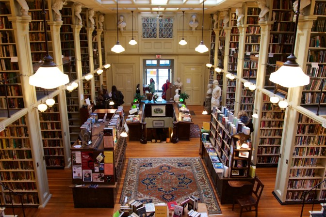 Main hall of library, with rows of bookshelves on either side of a large open area in the middle. Marble busts rest on shelves at the top of each bookshelf.
