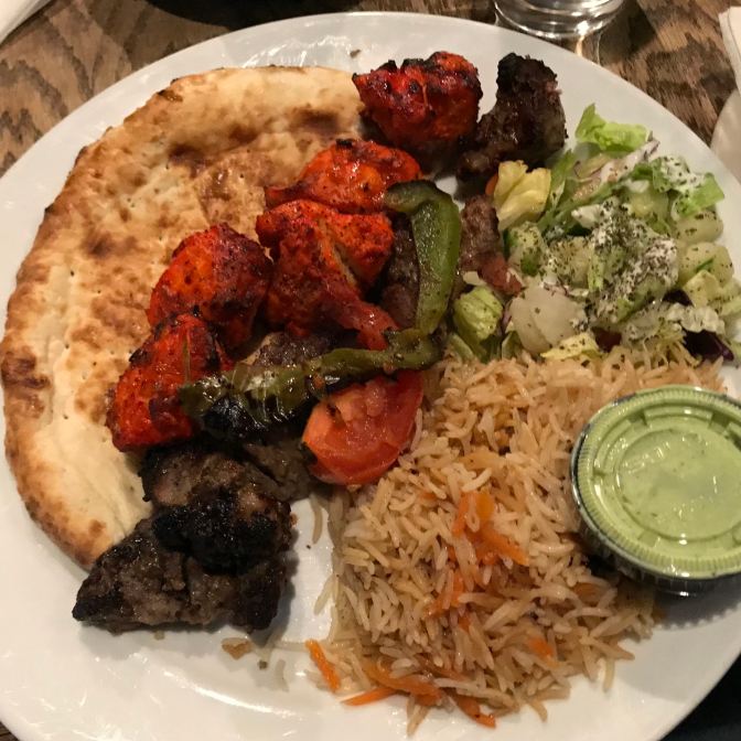 Chicken and beef kabob, with pita bread, vegetables, and rice, on a white plate.
