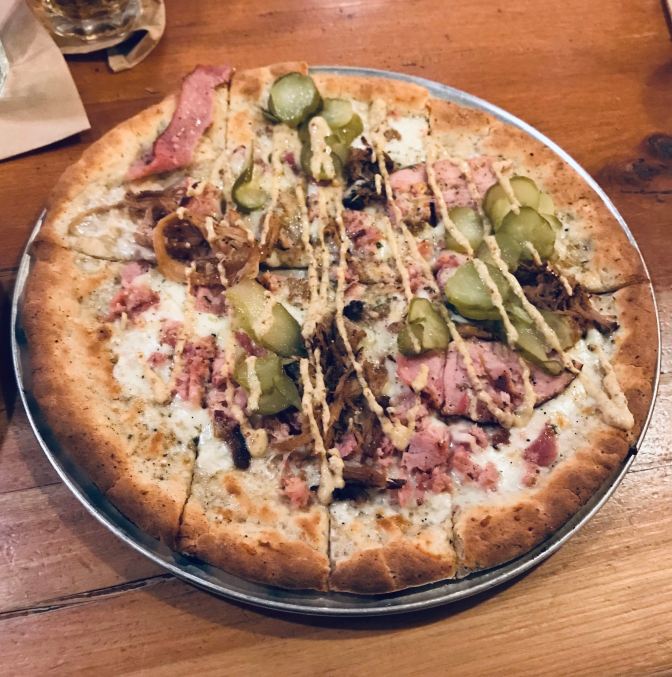 Cuban pizza with ham, pickles, cheese, and mustard on a flatbread crust.