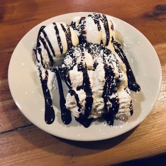 Brownie and ice cream sundae, with chocolate sauce and whipped cream, on a white plate.