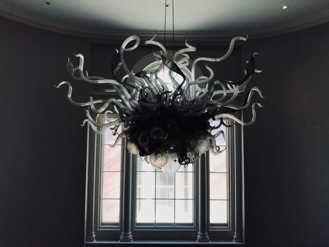 Glass chandelier with tentacles emerging from the top and glass globes in black netting at the bottom. A window is installed on the far wall.