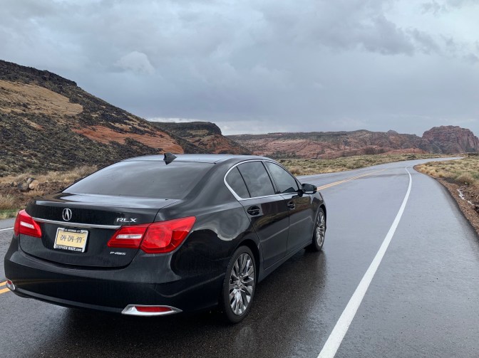 2016 Acura RLX black on rain-covered road with mountains in the background.