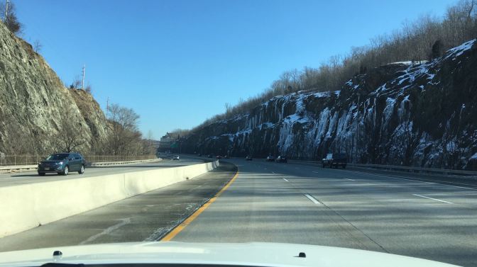 View of highway with rock cliffs on either side of the road, and ice covering the cliffs on the right.