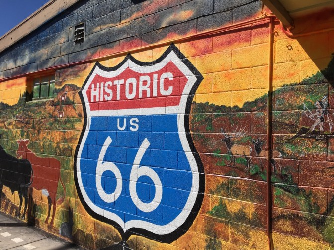 Mural of Route 66 sign on side of building with mural of Native Americans hunting bison.