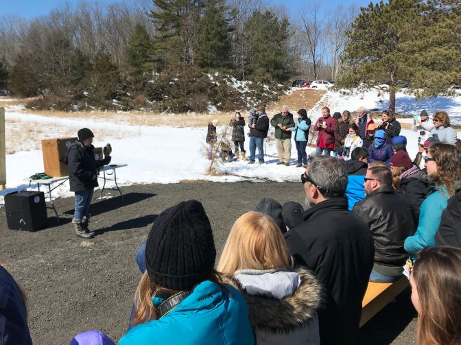 Crowd of people in a half-circle around a member of the Audubon Society holding a hawk.