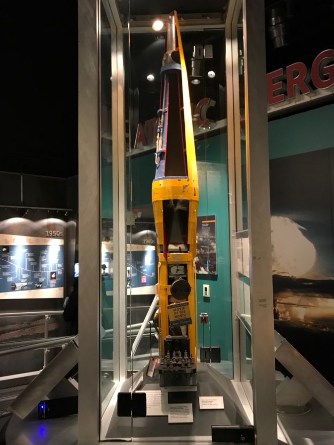 Yellow rocket, with panels removed, behind glass case.