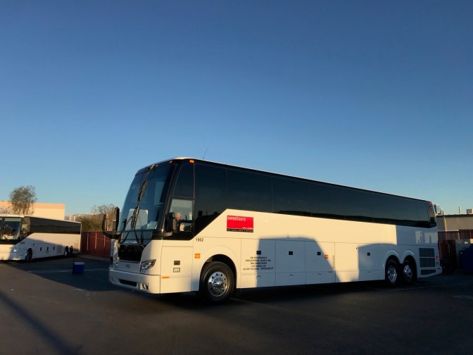 White and black tour bus in a parking lot.