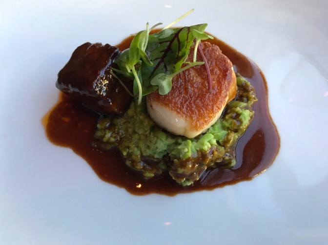 Scallop and pork belly on a bed of sweet pea and scallop sherry au jus.