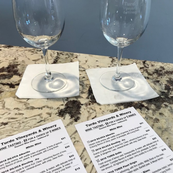 Two wine glasses on bar top with tasting menus in the foreground.