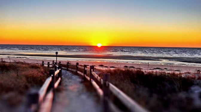 Beach sunset photo with path through dunes in foreground.
