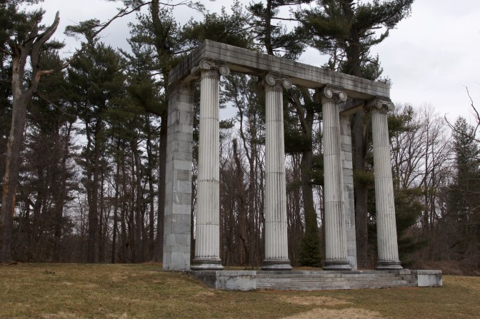 The Colonnade, a structure of four columns and two stone pillars, by the tree line.
