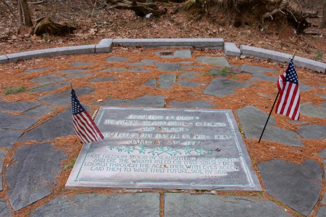 Grave marker memorial for unknown soldiers, surrounded by two American flags. A circle of stones surrounds the marker.