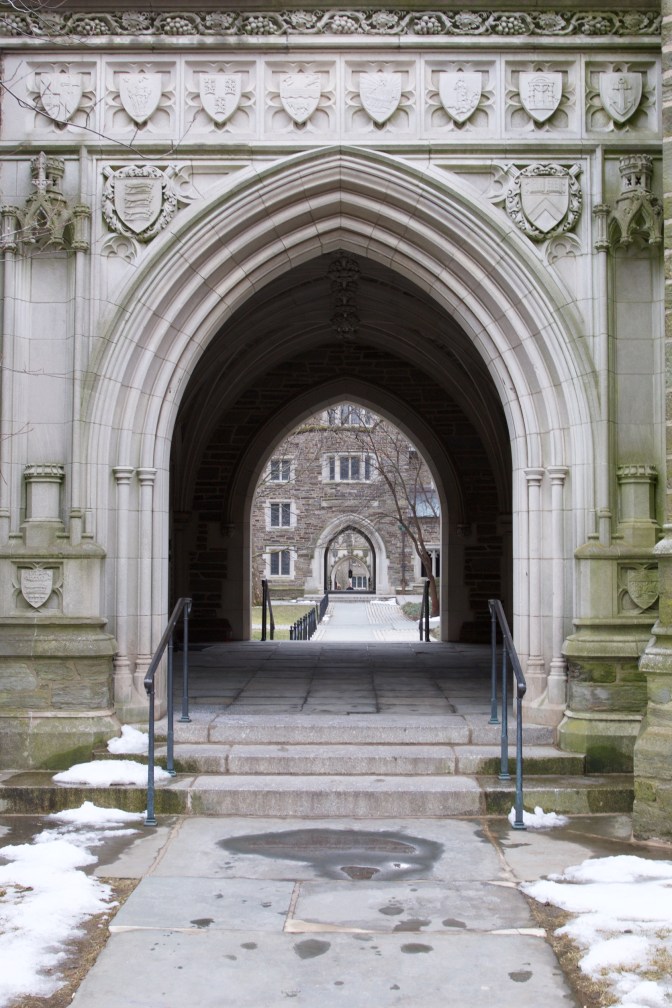 Gothic archway through building, looking at campus beyond.